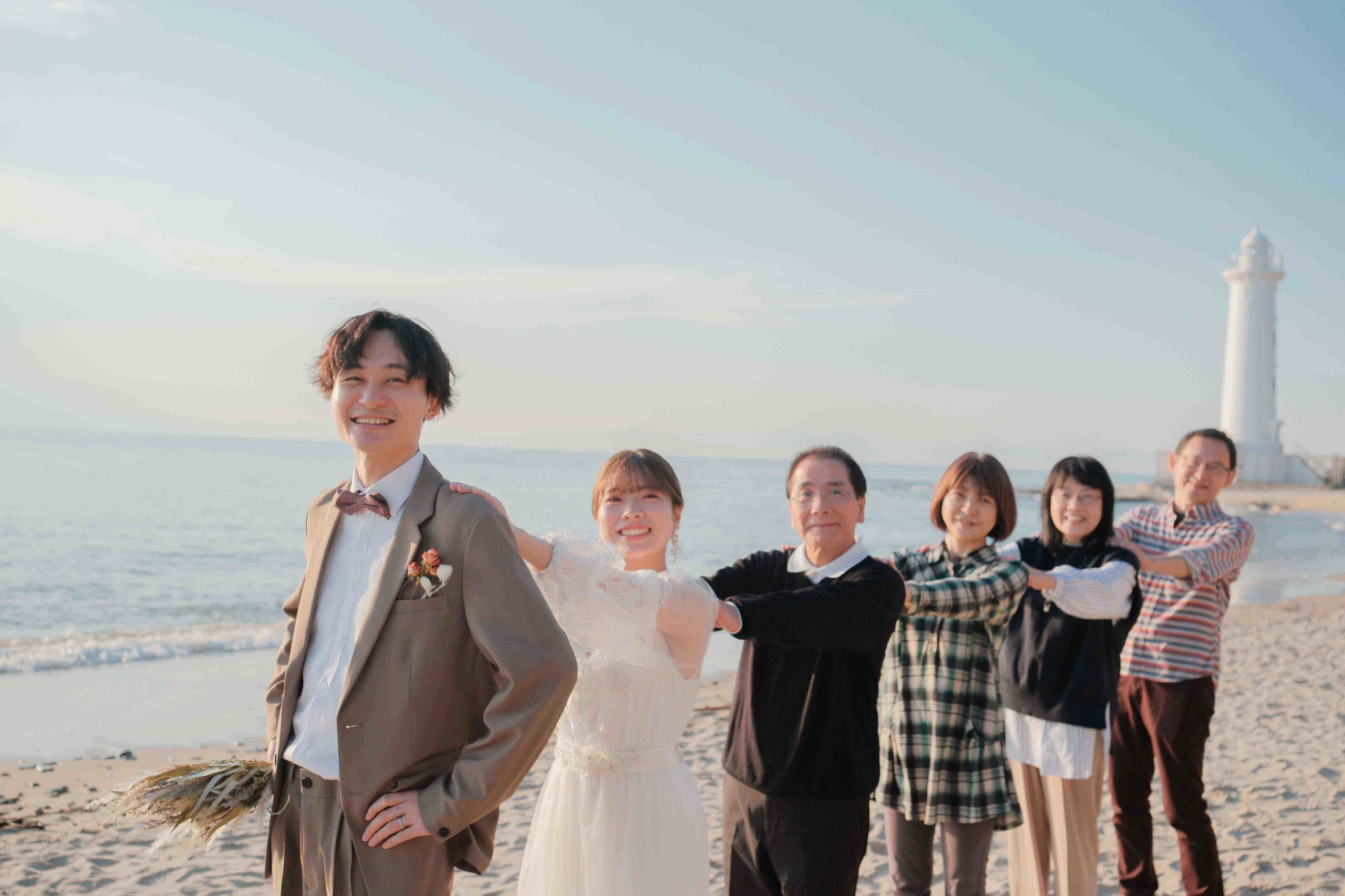 alt="野間灯台でビーチ前撮りをする笑顔の新郎新婦"