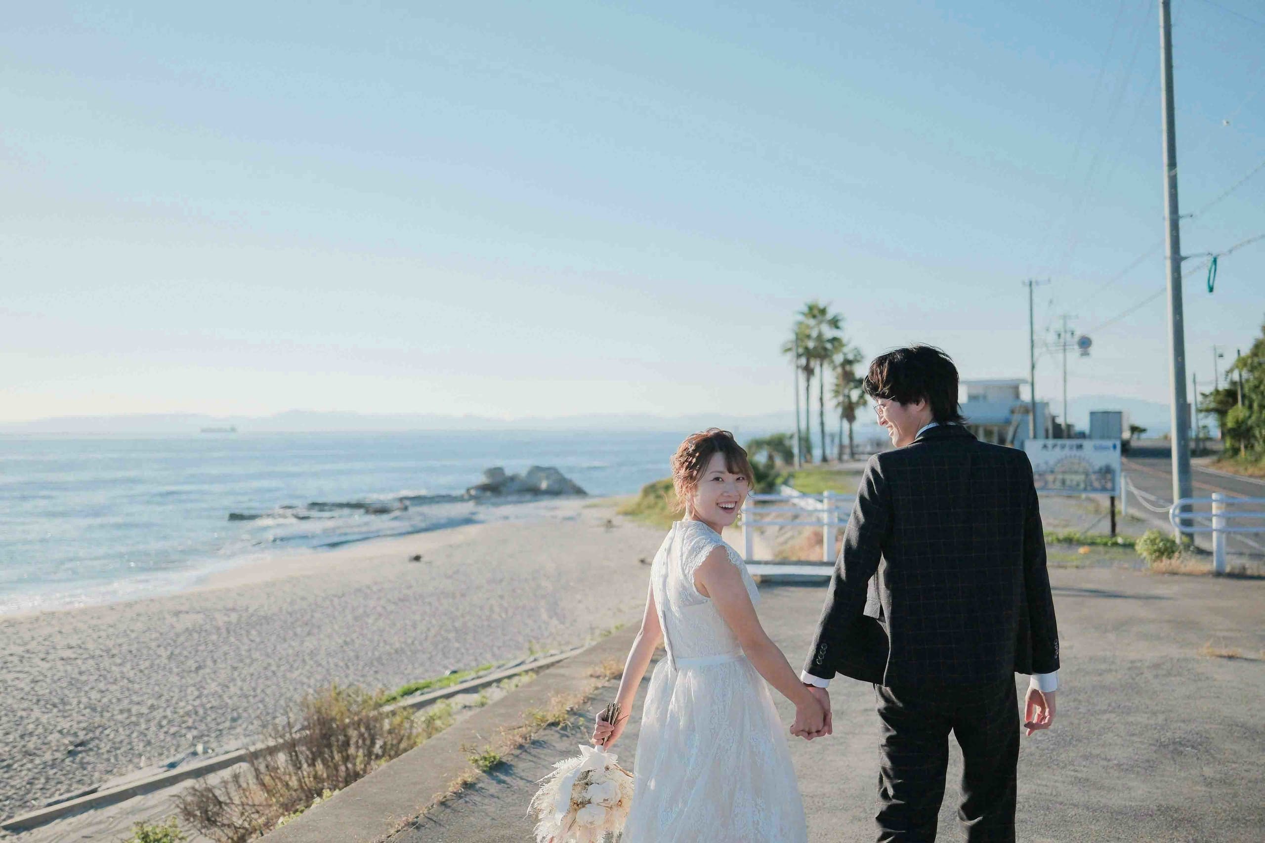 alt="野間灯台でビーチ前撮りをする笑顔の新郎新婦"