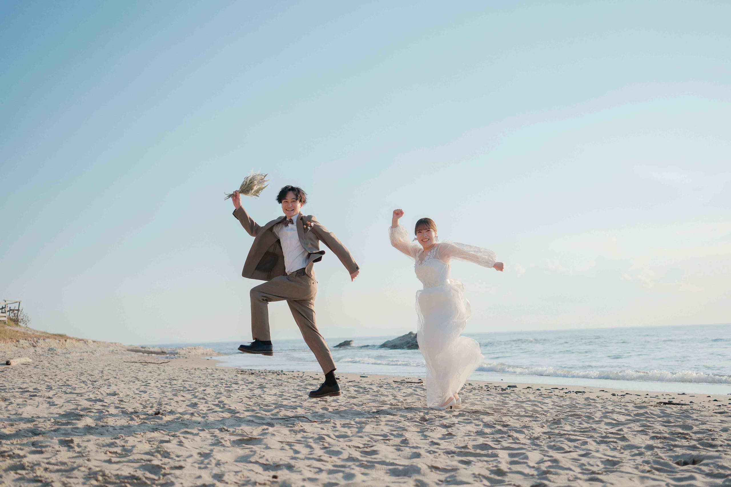 alt="野間灯台でビーチ前撮りをする笑顔の新郎新婦"