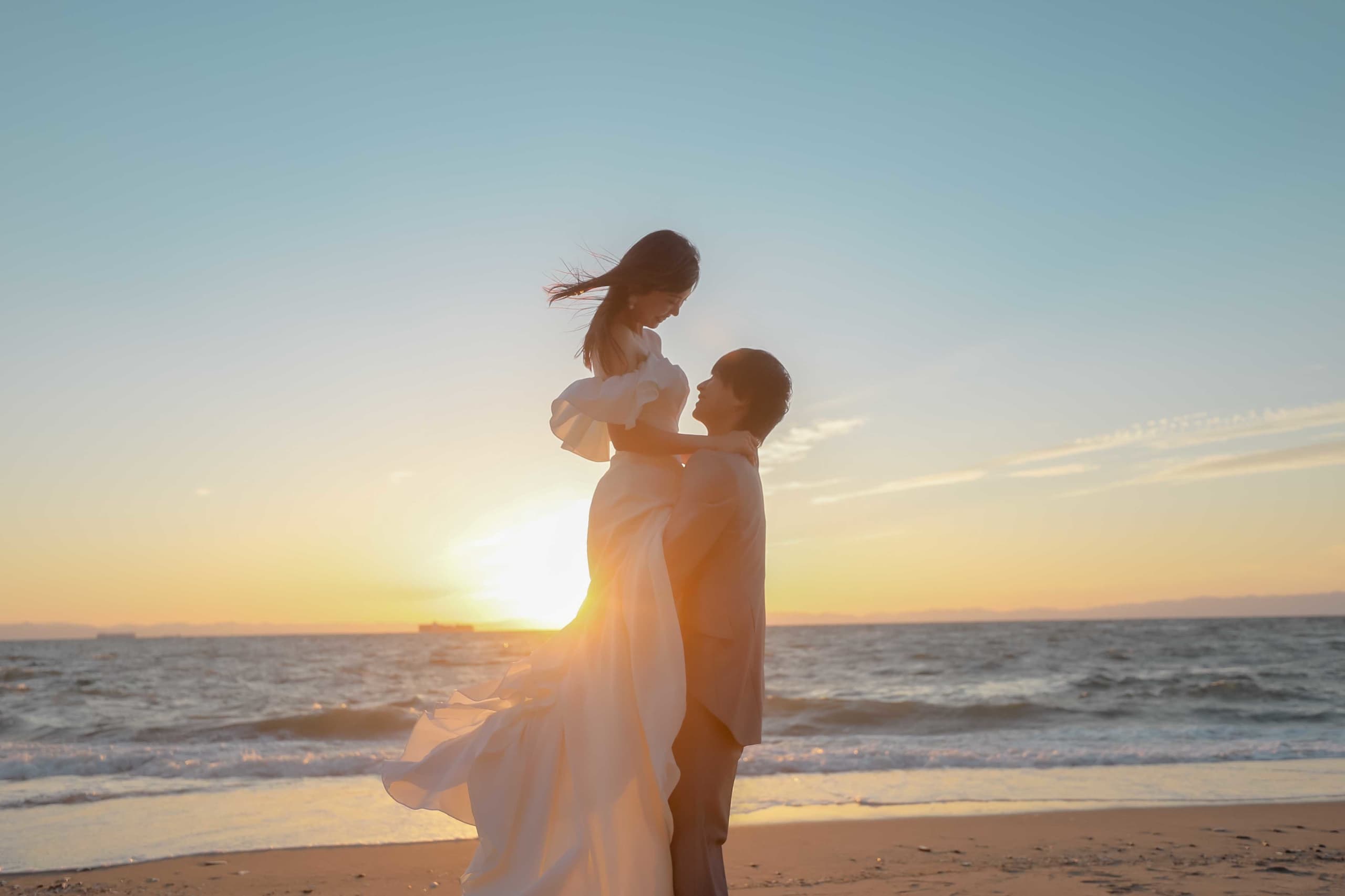 alt="野間灯台でビーチ前撮りをする笑顔の新郎新婦"