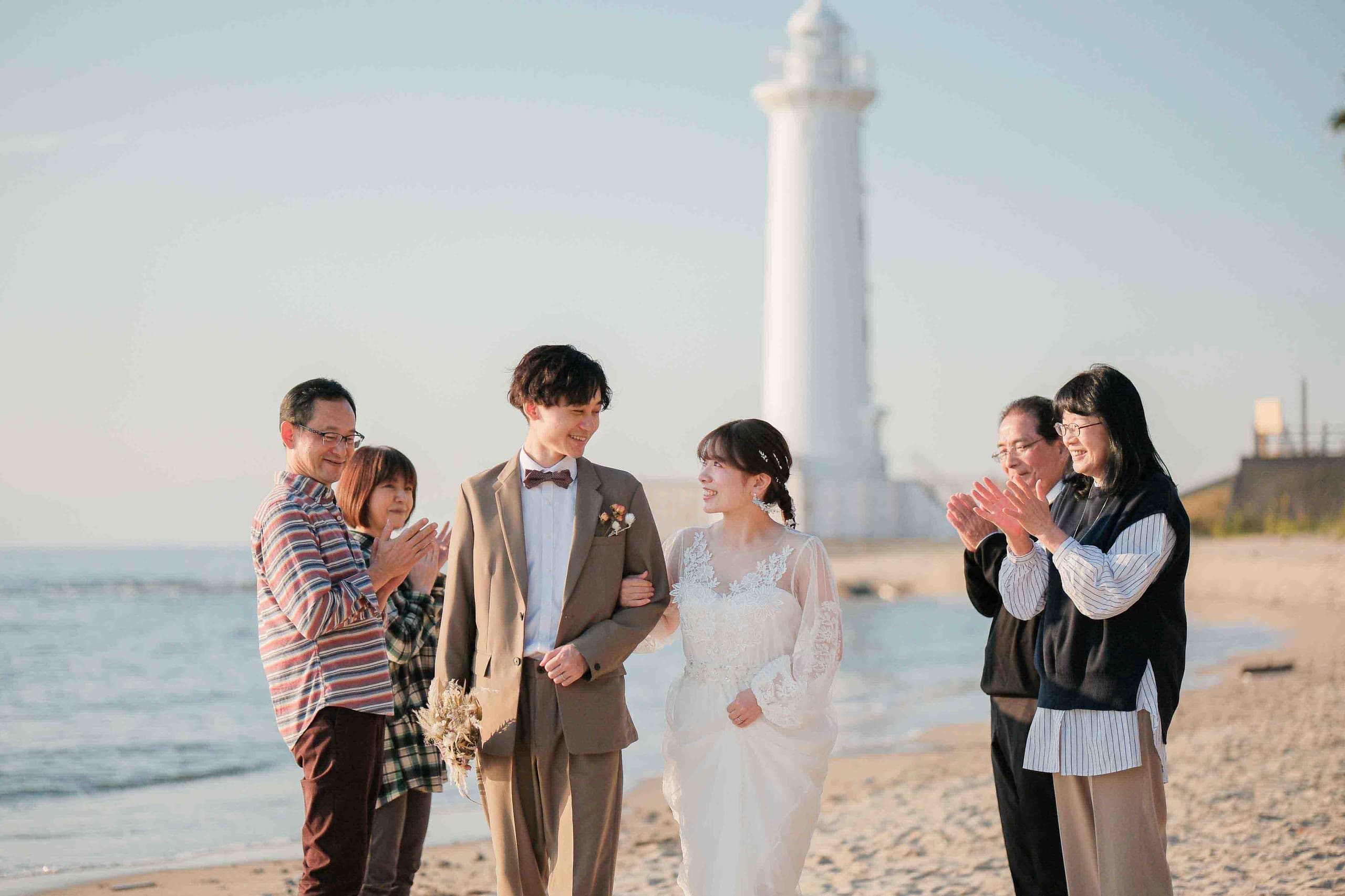 alt="野間灯台でビーチ前撮りをする笑顔の新郎新婦"
