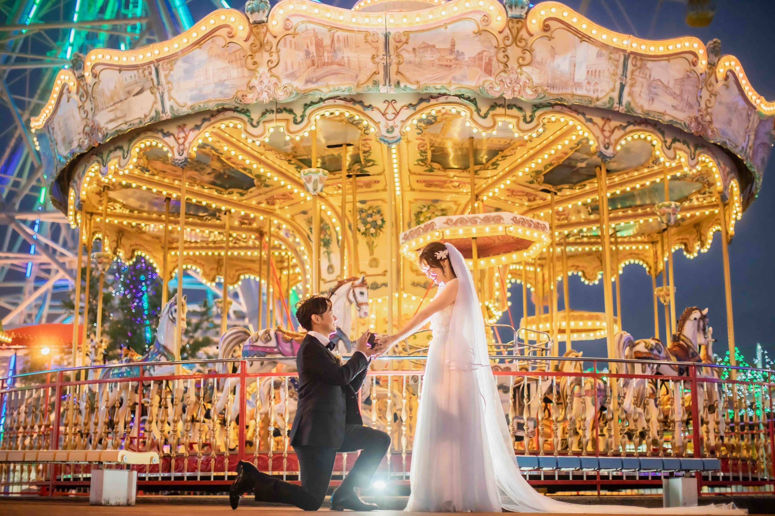 alt="夜の遊園地でナイトドレス前撮りをする笑顔の新郎新婦"