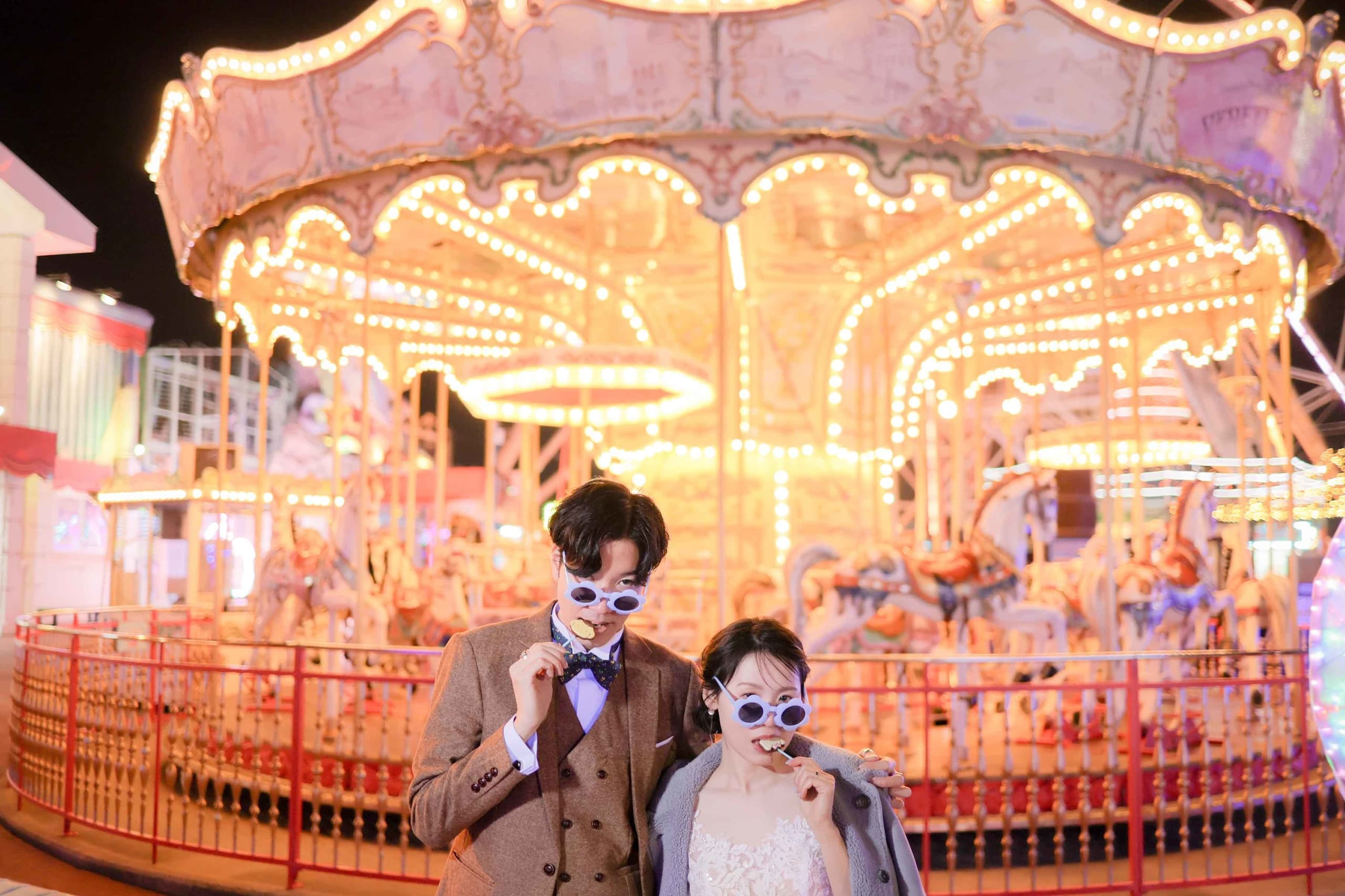 alt="夜の遊園地でナイトドレス前撮りをする笑顔の新郎新婦"