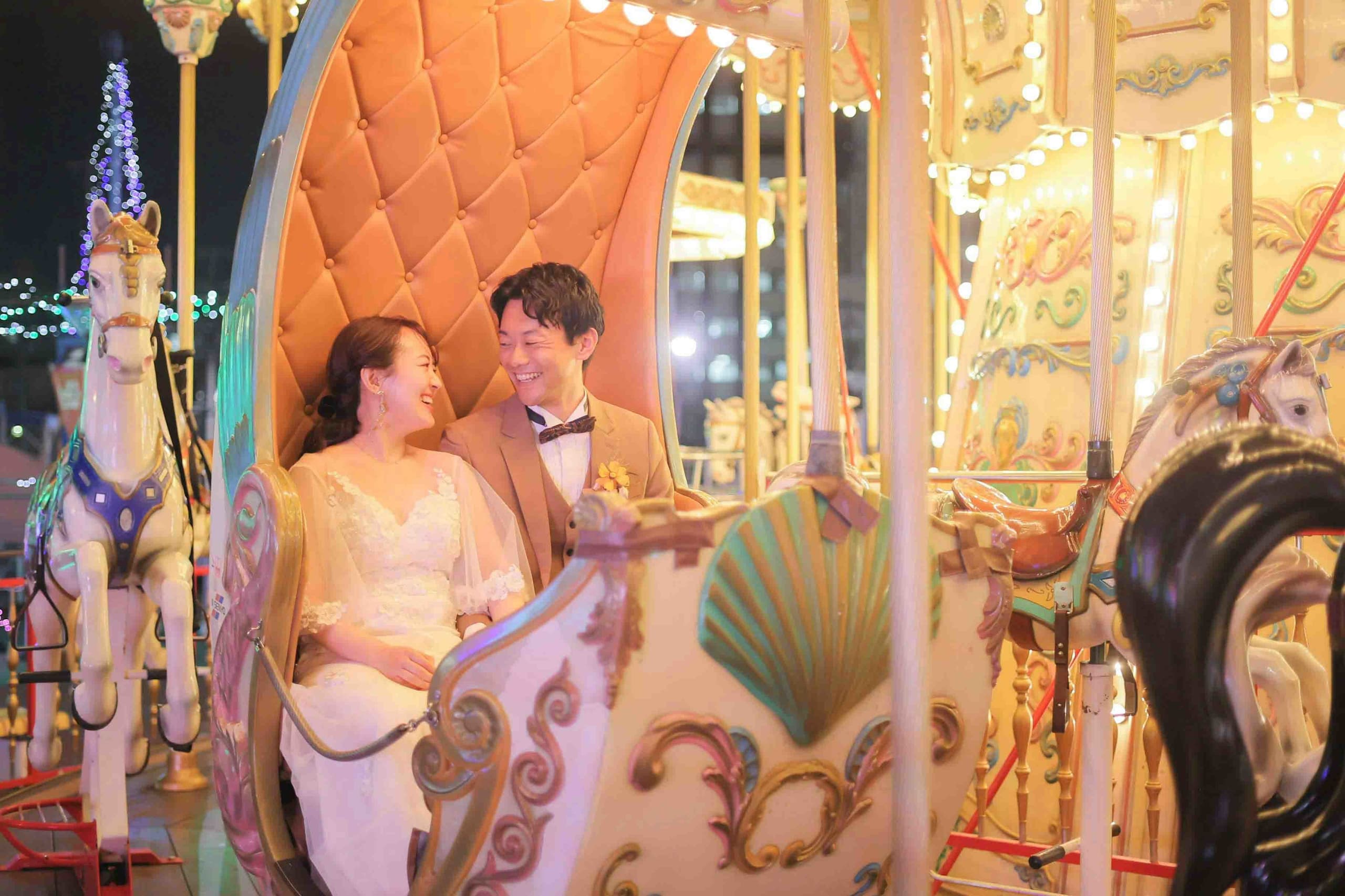 alt="夜の遊園地でナイトドレス前撮りをする笑顔の新郎新婦"